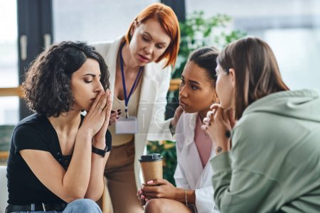 psychologue professionnel et de jeunes copines multiethniques regardant déprimé femme multiraciale assis avec les yeux fermés et les mains près du visage dans la salle de consultation, concept de résolution de problèmes