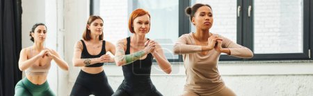 mindfulness and inspiration, diverse group of multicultural women looking forward while meditating with clenched hands during yoga class, harmony and mental health concept, banner