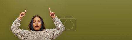 Schockiertes Preteen-Kind mit farbigen Haaren, das einen modernen Strickpullover trägt, während es in die Kamera schaut und mit den Fingern auf grün zeigt, Banner, modebewusste Preteen mit Sinn für Stil