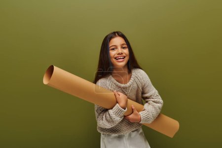 Photo for Cheerful and trendy brunette girl with dyed hair wearing modern knitted sweater holding rolled paper and looking at camera isolated on green, stylish girl in cozy fall attire concept - Royalty Free Image