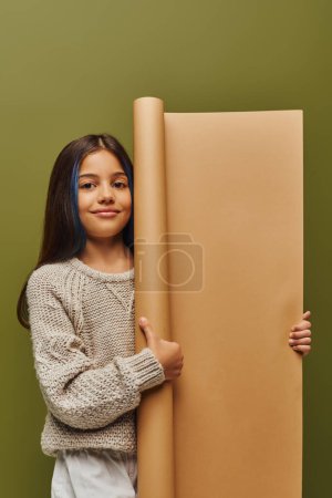 Photo for Smiling and trendy preadolescent girl with dyed hair wearing knitted sweater and autumn outfit and holding rolled paper isolated on green, autumn fashion for preteens concept - Royalty Free Image
