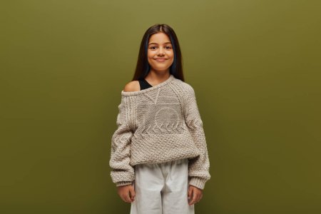 Portrait of positive preadolescent girl with colored hair wearing summer knitted sweater and looking at camera while standing isolated on green, relaxed autumn vibes concept 