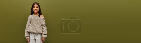 Foto de Chica morena preadolescente de moda en jersey de punto y traje de otoño mirando a la cámara mientras está de pie y posando aislado en verde, relajado concepto de vibraciones de otoño, pancarta - Imagen libre de derechos