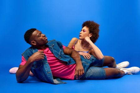 Photo for Thoughtful young african american best friends in bright and stylish summer outfits looking at each other while posing on blue background, fashionable besties radiating confidence, friendship - Royalty Free Image