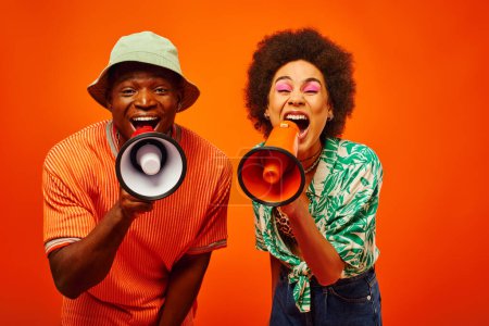 Photo for Excited young and stylish african american best friends in summer outfits screaming at loudspeakers while looking at camera together isolated on red, friends in fashionable outfits, friendship - Royalty Free Image