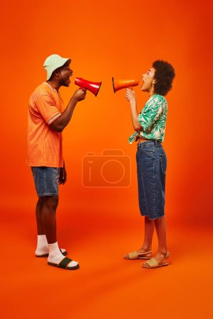 Téléchargez les photos : Vue latérale de jeunes excités afro-américains meilleurs amis dans des tenues d'été élégantes crier tout en tenant des haut-parleurs tout en se tenant debout sur fond rouge, amis dans des tenues à la mode - en image libre de droit