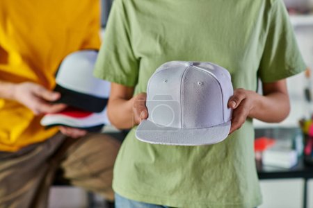 Photo for Cropped view of young african american designer holding snapback while standing near blurred colleague and working in print studio, sustainable business model concept - Royalty Free Image