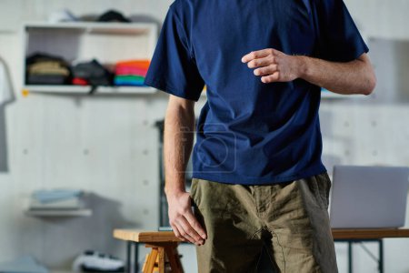 Cropped view of young craftsman in casual clothes standing near working table in blurred print studio at background, hands-on entrepreneurship concept 