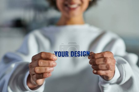 Photo for Cropped view of blurred and cheerful young african american artisan in sweatshirt holding printing layer with your design lettering in print studio, focused business owner managing workshop - Royalty Free Image