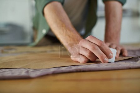 Photo for Cropped view of blurred young craftsman holding chalk and marking fabric near sewing pattern on table in sprint studio, multitasking business owner managing multiple project - Royalty Free Image