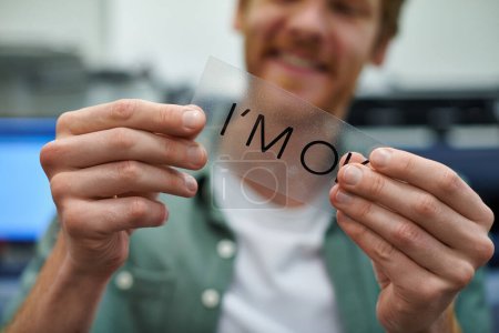 Cropped view of young blurred craftsman holding printing layer with I'm ok lettering in print studio, small business owner working on project, close up, creative process, workflow 