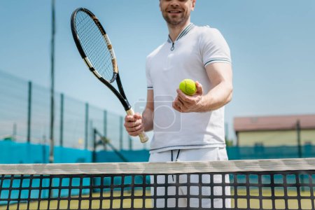 przycięty widok człowieka w odzieży sportowej trzyma rakietę tenisową i piłkę w pobliżu sieci, gracz, hobby i sportu