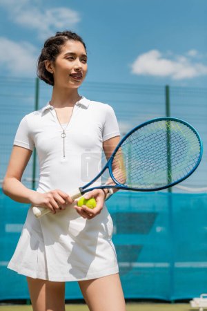 szczęśliwa kobieta w aktywnym ubraniu trzyma rakietę tenisową i piłkę, gracz na korcie, sport i motywacja