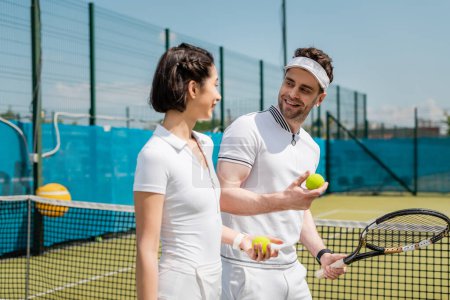 homme et femme positifs tenant balles de tennis et raquette sur le court, passe-temps et loisirs