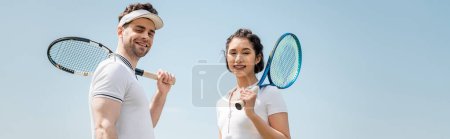 banner, happy couple in sportswear standing with tennis rackets on court, looking at camera, sport