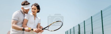 banner, cheerful man teaching girlfriend how to play tennis on court, holding rackets and ball