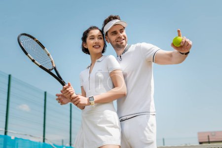 szczęśliwy człowiek wskazując daleko od dziewczyny na korcie tenisowym, trzymając rakiety, sport i romans