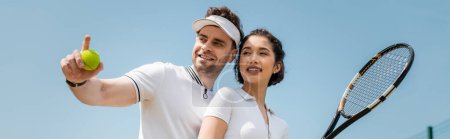 banner, happy man pointing away near girlfriend on tennis court, holding racket, sport and romance