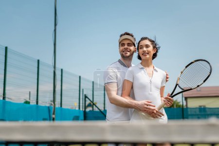 romance on tennis court, happy man teaching girlfriend how to play tennis, summer sport
