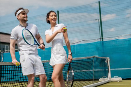 Foto de Mujer feliz señalando lejos, hombre sonriendo y sosteniendo raqueta de tenis, verano, deporte de pareja, pasatiempo - Imagen libre de derechos
