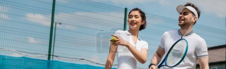Téléchargez les photos : Bannière, femme heureuse pointant du doigt, homme souriant et tenant une raquette de tennis, été, sport de couple - en image libre de droit
