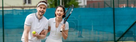 Foto de Pancarta, alegre pareja en ropa activa sosteniendo raquetas y pelota cerca de la red de tenis, pasatiempo y deporte - Imagen libre de derechos