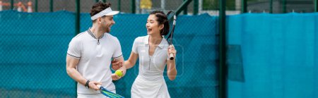 Foto de Pancarta, alegre pareja en ropa activa sosteniendo raquetas, caminando en pista de tenis, pasatiempo y deporte - Imagen libre de derechos