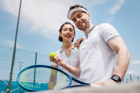 pozytywna para patrząca w kamerę, rakietę tenisową i piłkę, aktywność latem, czas wolny i zabawa