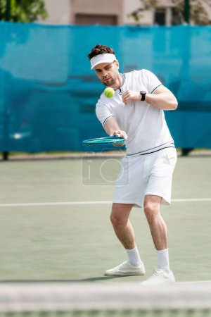 Hüpfender Tennisball, gutaussehender Tennisspieler, der auf dem Platz übt, Schläger in der Hand, Sport und Freizeit