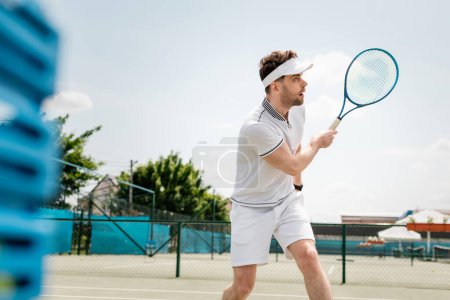 schöner Tennisspieler mit Sportvisier, Schläger in der Hand und Tennis auf dem Platz, Motivation