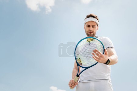 healthy lifestyle, handsome man in visor cap looking at tennis racquet on court, sport and hobby