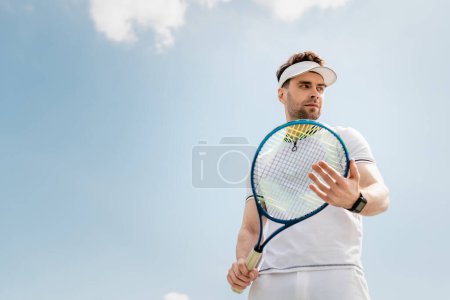 Foto de Estilo de vida saludable, hombre guapo en desgaste activo y gorra de visera con raqueta de tenis en la cancha - Imagen libre de derechos