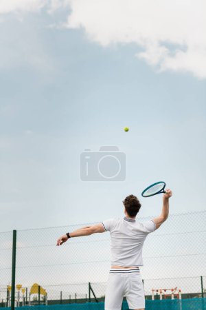 Photo for Back view of man playing tennis on court, holding racket, hitting ball, backhand - Royalty Free Image