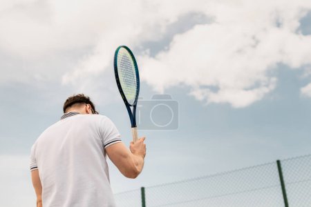 Rückansicht des sportlichen Mannes mit Tennisschläger auf dem Platz gegen den Himmel, Motivation, Sport