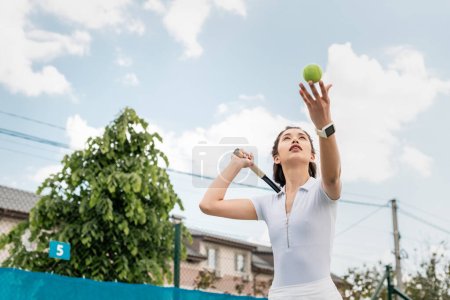 Photo for Low angle view of sportswoman hitting the ball while playing tennis, holding racket, motivation - Royalty Free Image