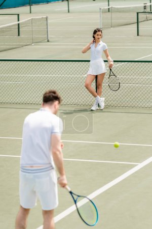 woman standing near tennis net and holding racket, man in active wear on blurred foreground magic mug #665314670