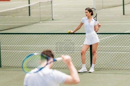 Photo for Female tennis player standing near net and holding racket, man in active wear on blurred foreground - Royalty Free Image