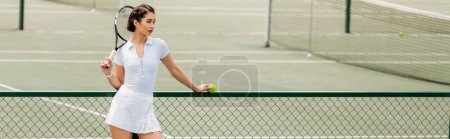 sportswoman in white active wear holding ball and racket while standing near tennis net, banner