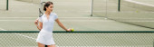 sportswoman in white active wear holding ball and racket while standing near tennis net, banner magic mug #665314686