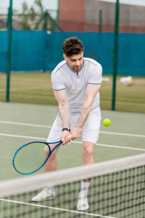 przystojny tenisista trzymając rakietę i uderzając piłkę tenisową na korcie, sport jako hobby