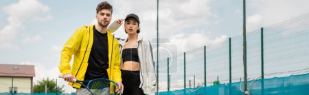 Foto de Pancarta, pareja de moda de pie en la cancha de tenis con raquetas, hombre y mujer en ropa deportiva - Imagen libre de derechos