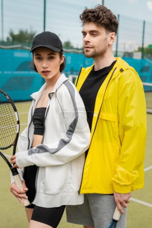 sport, modny mężczyzna i kobieta stojący na korcie z rakietą tenisową, sportowa para, hobby