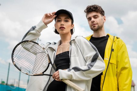sport, man and woman standing on court with tennis racquet, stylish couple in sporty jackets, hobby