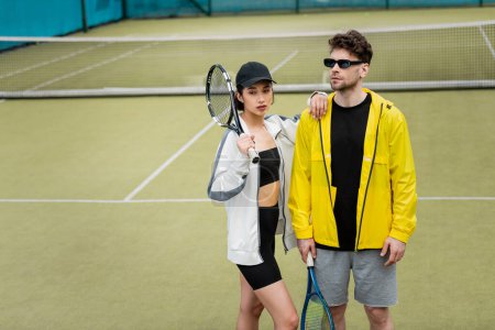 styl i sport, sportowa para, mężczyzna w okularach przeciwsłonecznych i kobieta w czapce z rakietami na korcie tenisowym
