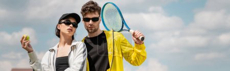 banner, hobby and sport, stylish man and woman in sunglasses holding racket and ball on tennis court