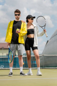 couple sport, hobby, stylish man and woman in sunglasses holding rackets and ball on tennis court Stickers #665315124