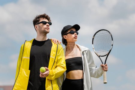 tenis sport i moda, mężczyzna i kobieta w okularach przeciwsłonecznych trzyma rakietę i piłkę na korcie tenisowym, hobby