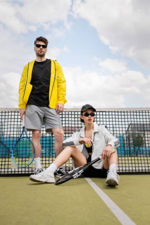 Photo for Couple sport, man and woman in sunglasses posing on tennis court with rackets, athletes fashion - Royalty Free Image