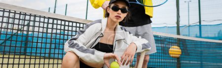 baner, kobieta w okularach przeciwsłonecznych i czapce pozującej blisko mężczyzny, rakieta do piłki i tenisa, aktywne ubranko
