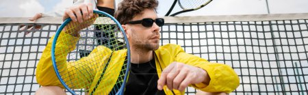 bannière, homme en lunettes de soleil et port actif tenant raquette près de la femme et filet de tennis, mode sportive
